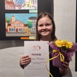 Lauma Perševica pie sava darba ar diplomu rokās.